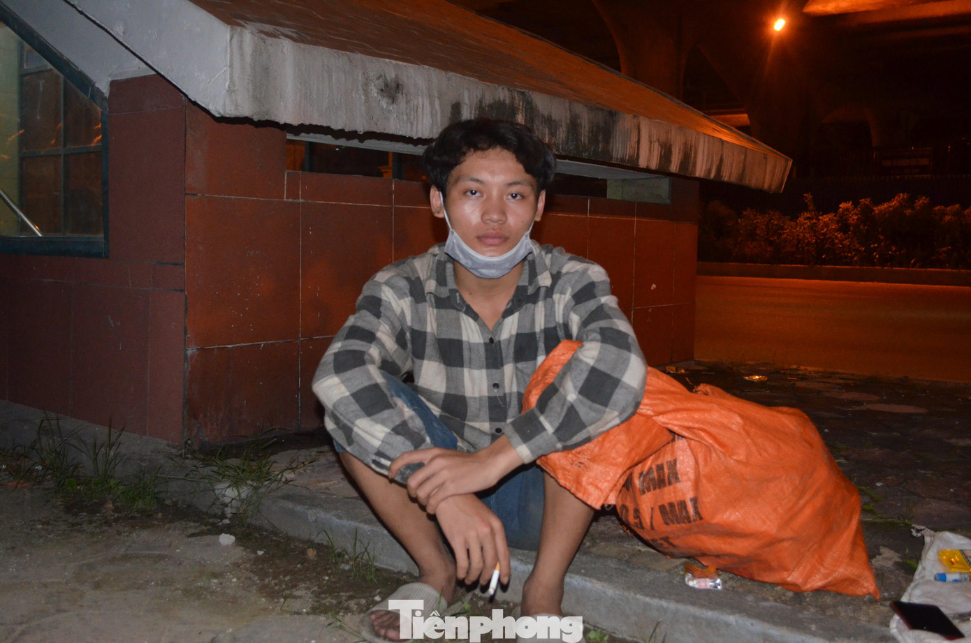 Đạt cho biết, lúc mới lên Hà Nội, em ở trọ cùng một người bạn mới quen. Tuy nhiên, mới ở một đêm, hôm sau ngủ dậy cả ví tiền, điện thoại, quần áo, giấy xét nghiệm COVID-19 bị lấy cắp mất cả. Đạt đành phải ra gầm cầu ở và hàng đêm đi nhặt phế liệu để hôm sau bán lấy tiền mua mỳ tôm sống qua ngày. Dưới gầm cầu đường vành đài 3 dọc quốc lộ 1A (đoạn gần bến xe Nước Ngầm) là nơi trú ngụ của ba người đàn ông khác đến từ Nam Định, Điện Biên và Nghệ An. Hàng ngày, họ trông chờ vào những suất cơm từ thiện, nếu không thì nhai mỳ tôm sống. Mọi sinh hoạt cá nhân, sạc pin điện thoại, họ nhờ các nhà dân gần đó trợ giúp. Anh Lô Văn Cà Huệ (quê huyện Quế Phong, tỉnh Nghệ An) tâm sự, anh lên Hà Nội tìm việc từ đợt Tết 2021. Công việc cơ khí dân dụng bên quận Long Biên của anh vẫn suôn sẻ đến khi Hà Nội thực hiện những biện pháp thắt chặt để phòng chống dịch. “Tôi đi làm lương được 5 triệu đồng/tháng. Đóng tiền trọ 1 tháng hết khoảng 1,2 triệu đồng, giờ mất việc tôi ra đây với anh em cho tiết kiệm tiền trọ”, thanh niên người dân tộc Thái chia sẻ. Trình duyệt của bạn không hỗ trợ hiển thị video. Clip: Đinh Quang Đạt kể về cuộc sống ngày ở gầm cầu, đêm nhặt rác của mình