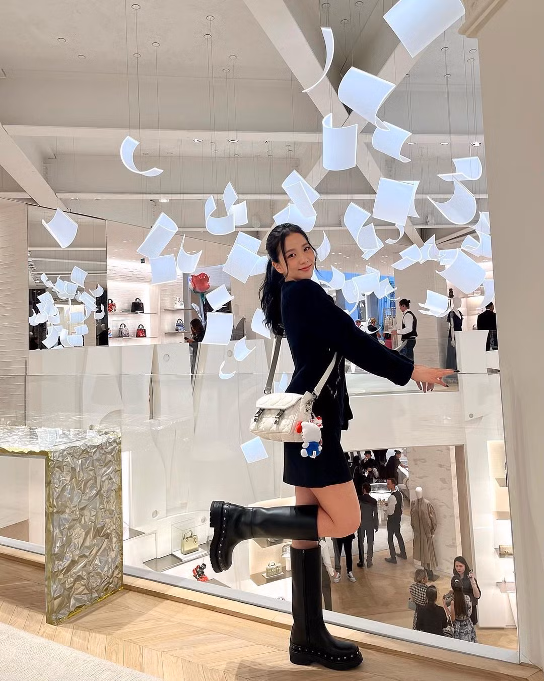 Jisoo tươi tắn tại cửa hàng Dior ở Paris, cô mặc áo len đan Kijun, bốt Diorquake và túi Diorcamp nhỏ có gắn thú nhồi bông Hello Kitty.