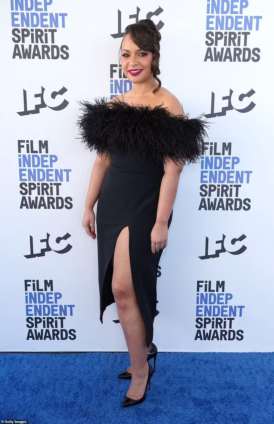 Jasmine Cephas-Jones mặc một chiếc váy đen ôm sát người với phần trên đính lông vũ và đường xẻ cao.