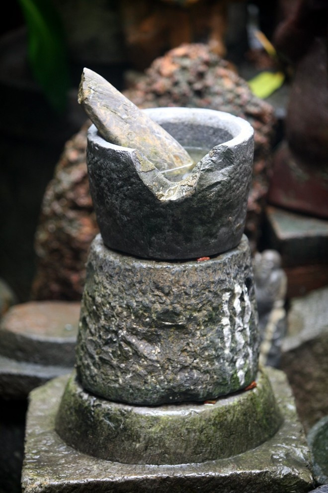 Một sự sắp đặt tạo hình gồm hai chiếc cối đá úp đáy vào nhau đặt trên phiến đã đá đỡ cột đình, chiếc chày đá này ở vị trí vốn có của nó 