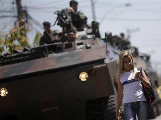 Một nữ sinh viên đi qua xe tăng của quân đội Brazil khi tuần tra tại khu ổ chuột Muquico ở Rio de Janeiro. 