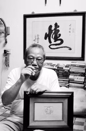 NSND Đào Trọng Khánh ôm bức ký họa của Văn Cao vẽ Nguyễn Tuân, phía sau là bức thư pháp chữ 