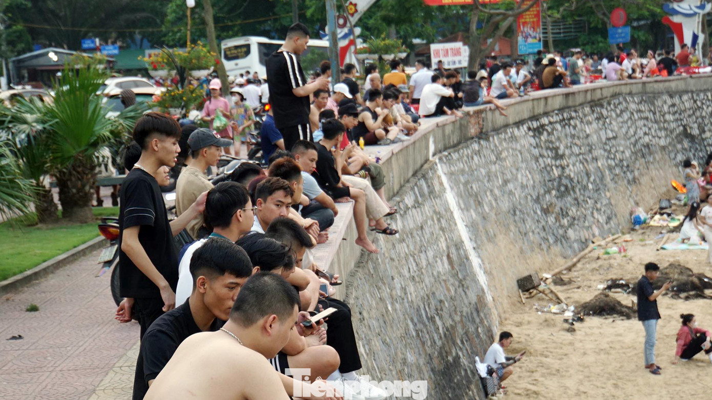 Nhiều người ngồi trên bờ kè chờ người thân tắm biển.