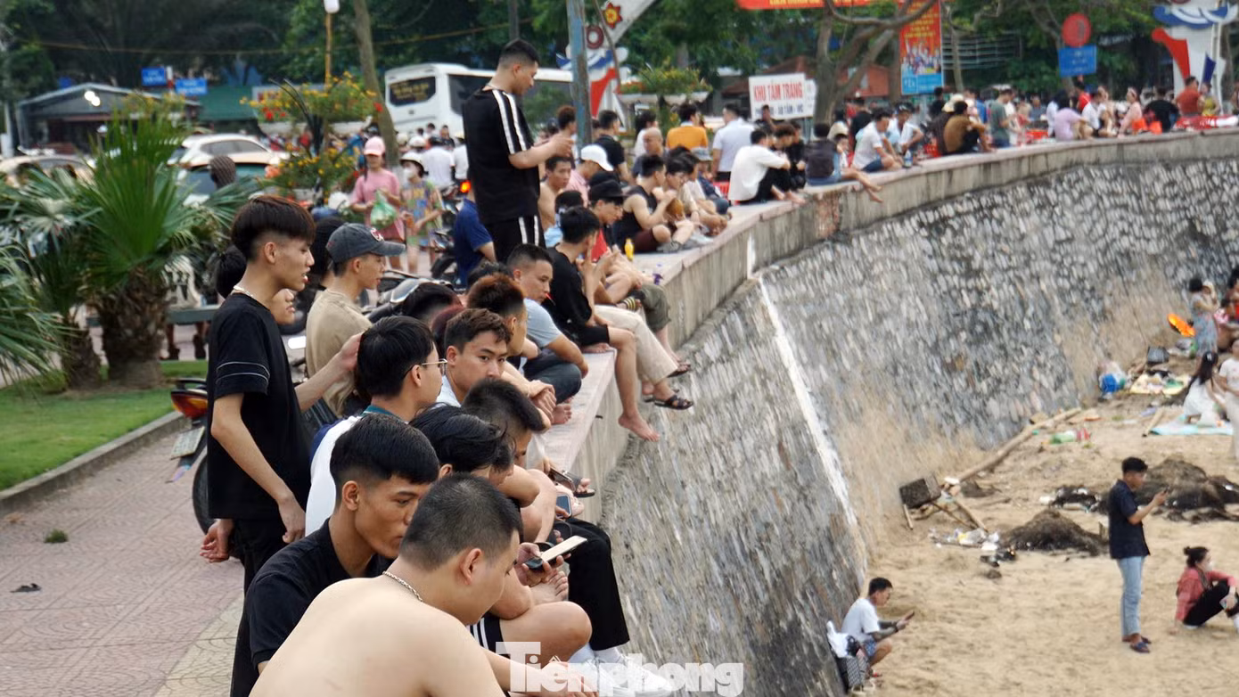 Nhiều người ngồi trên bờ kè chờ người thân tắm biển.