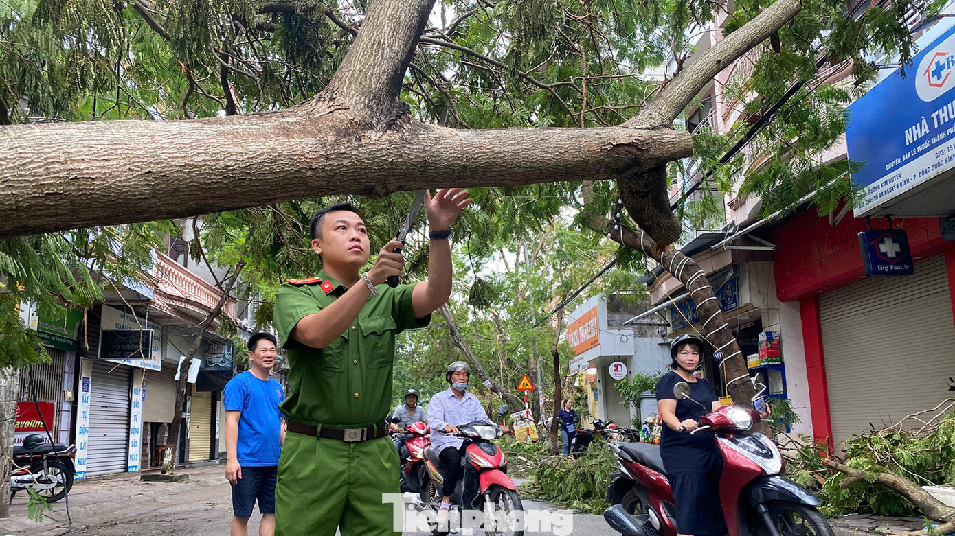 Công an phường Đổng Quốc Bình huy động cán bộ, chiến sĩ hỗ trợ lực lượng vệ sinh môi trường cưa cắt cành cây để thông đường tạm cho người dân di chuyển.