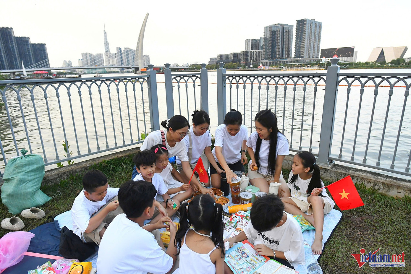 Chị Huyền Trinh (thứ hai từ phải qua) cho biết, gia đình chị gồm gần 20 người cả trẻ con, người lớn đã ra bờ sông chọn chỗ ngồi từ 15h. Tuy nhiên khu vực gần tượng đài Đức Thánh Trần đã chật kín, họ đành chọn một góc xa hơn để trải bạt, ăn tối chờ tới 21h30.