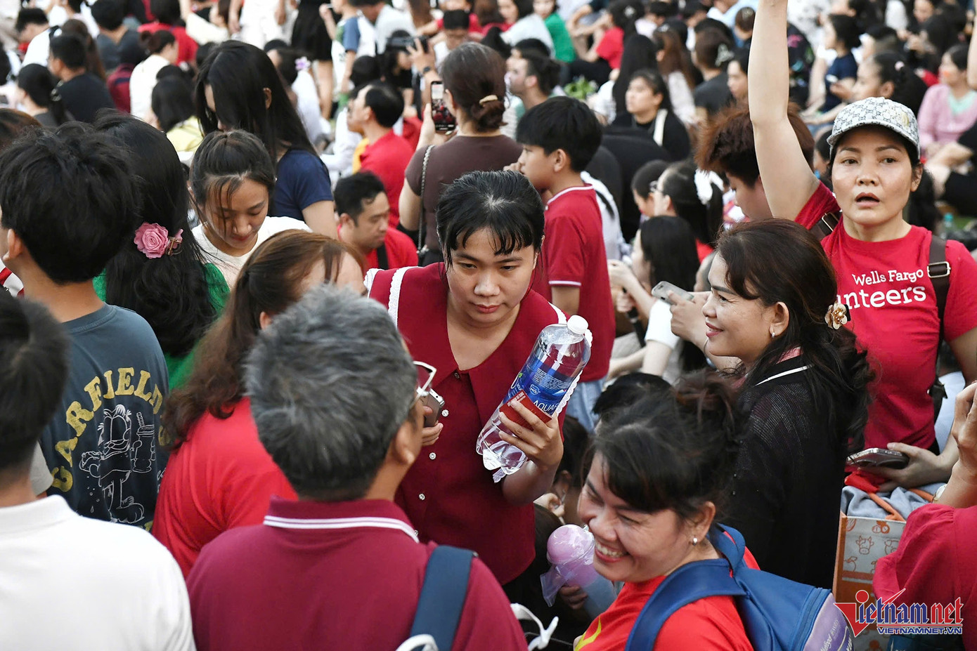 Một phụ nữ khó khăn di chuyển trong dòng người để tìm chỗ, trên tay chị cầm một chai nước lớn để tiếp sức cho cả buổi tối.