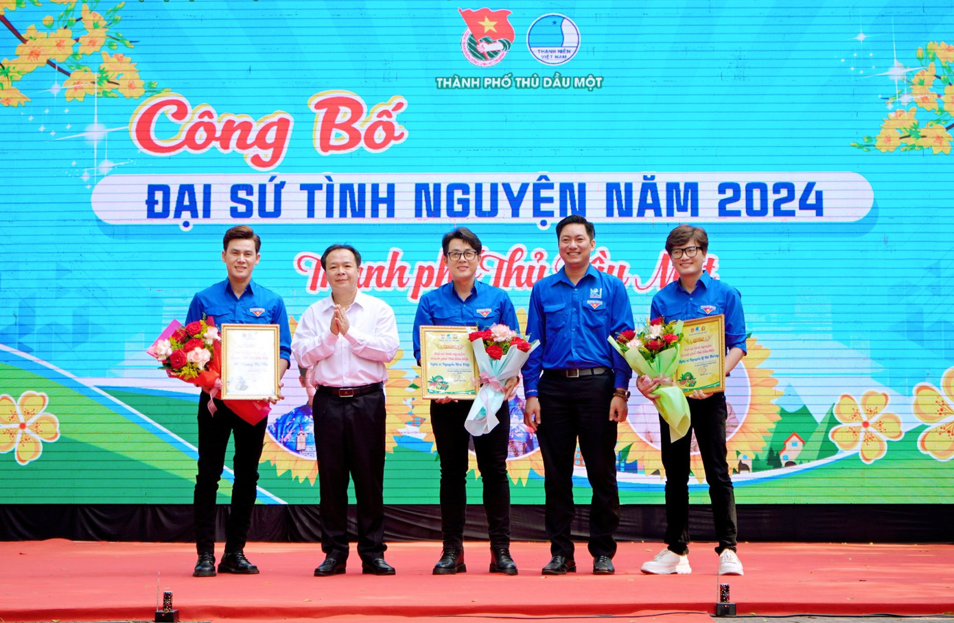 Ông Nguyễn Văn Đông - Bí thư Thành ủy Thủ Dầu Một (thứ hai từ trái sang) và anh Nguyễn Minh Tâm - Bí thư Thành Đoàn Thủ Dầu Một (thứ hai từ phải sang) tặng hoa cho các nghệ sĩ Nguyễn Hòa Hiệp, Nguyễn Lê Bá Thắng và MC Phùng Thế Phi là đại sứ tình nguyện.
