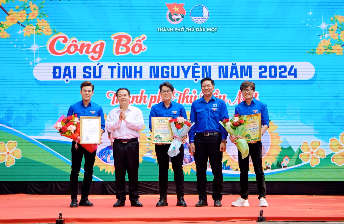 Ông Nguyễn Văn Đông - Bí thư Thành ủy Thủ Dầu Một (thứ hai từ trái sang) và anh Nguyễn Minh Tâm - Bí thư Thành Đoàn Thủ Dầu Một (thứ hai từ phải sang) tặng hoa cho các nghệ sĩ Nguyễn Hòa Hiệp, Nguyễn Lê Bá Thắng và MC Phùng Thế Phi là đại sứ tình nguyện.