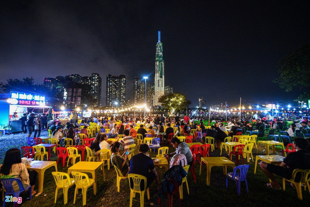 Từ 19h, khu ăn vặt cạnh bờ sông Sài Gòn (TP Thủ Đức, TP.HCM) bắt đầu nhộn nhịp. Hàng chục dãy bàn ghế được kê ngoài trời để khách ngồi ăn uống, hóng gió.