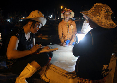 Thương lái ngồi tại chợ cá, tập trung chỗ có ánh đèn để tính tiền