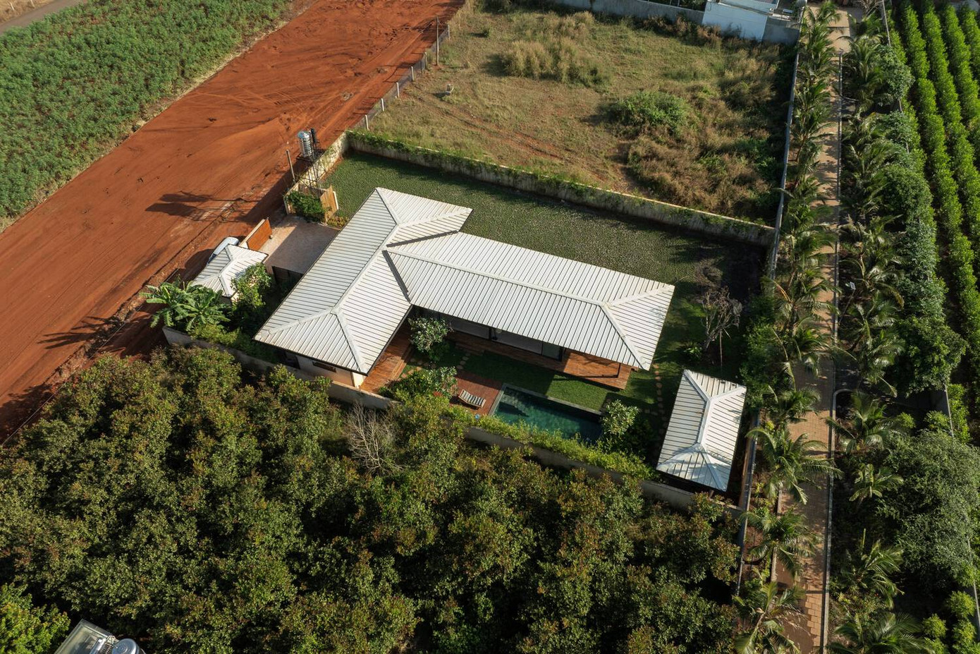 Hai khối nhà bao gồm phòng ngủ và phòng khách ghép với nhau tạo thành hình chữ T hướng ra con đường đất.