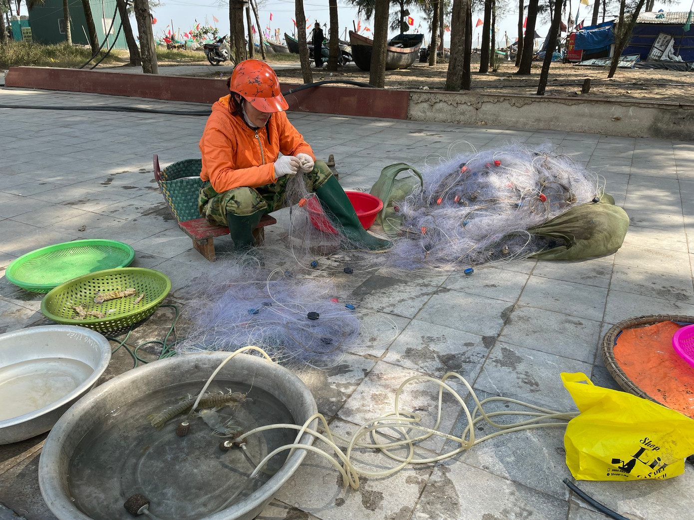 Tôm cá tươi mắc lưới vừa được đưa từ tàu thuyền lên bờ. Các hộ gia đình ngư dân vừa tháo gỡ cá tôm khỏi lưới vừa bán cho khách.
