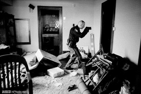 2008: Một nhân viên cảnh sát có vũ trang tiến vào khám xét một ngôi nhà đã bị bỏ hoang ở Cleveland, bang Ohio, Mỹ để tiến hành tịch thu tài sản, nhà đất theo giấy tờ thế chấp. Bức ảnh được chụp trong thời kỳ kinh tế Mỹ suy thoái nặng nề