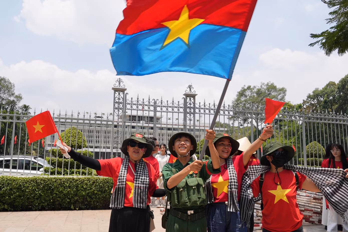 Người dân vẫy cờ Mặt trận Dân tộc Giải phóng miền Nam khi chụp ảnh trước Dinh Độc Lập ngày 29/4. (Ảnh: AP)