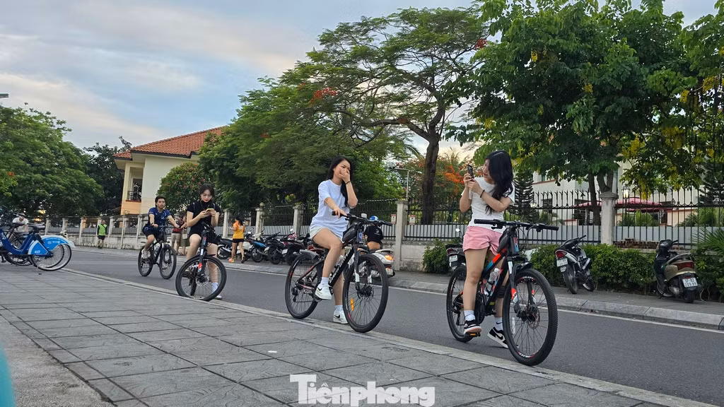 Các bạn trẻ đạp xe tập thể dục dừng chân ngắm vẻ đẹp hoàng hôn khi mặt trời lặn xuống phía bên kia mặt hồ.