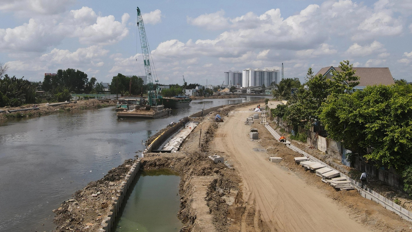 Trên công trường, các nhà thầu tăng tốc thi công đường giao thông ven kênh trong bối cảnh nguồn cát đắp nền rất khan hiếm. Để tránh cảnh &quot;bó gối đợi cát&quot;, liên danh nhà thầu thi công gói thầu xây lắp số 1 và số 2 đã linh hoạt bố trí hàng chục xe ủi, xe cuốc san gạt mặt đường và phân bổ công nhân thi công sàn giảm tải, khoan cọc nhồi, đúc các loại cấu kiện. Cùng lúc, hàng trăm công nhân được bố trí dọc tuyến lắp đặt hạng mục hố ga, hào kỹ thuật, cống thoát nước. Trong ảnh: Phần đường giao thông đoạn từ rạch Nước Lên đến cầu Đường C đã đắp cát, gần hoàn chỉnh hào kỹ thuật.