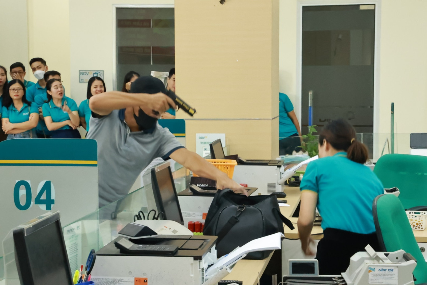 Tình huống giả định tên cướp bịt mặt, dùng súng uy hiếp, buộc nhân viên ngân hàng bỏ tiền vào ba lô.