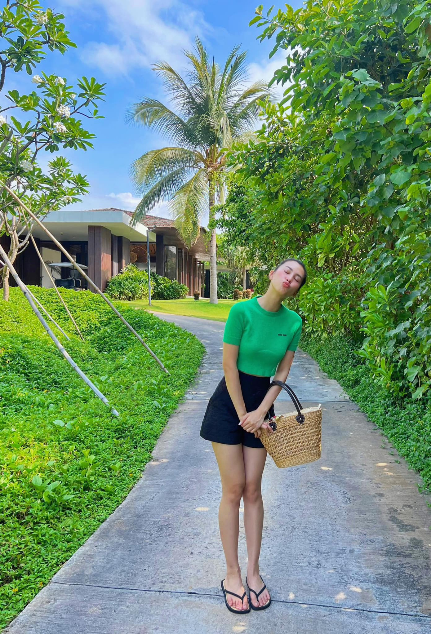 Hoa hậu Tiểu Vy chọn gam màu xanh lá nổi bật kết hợp với quần soóc lưng cao. Bộ đôi túi cói và dép cói được sử dụng hợp lý.