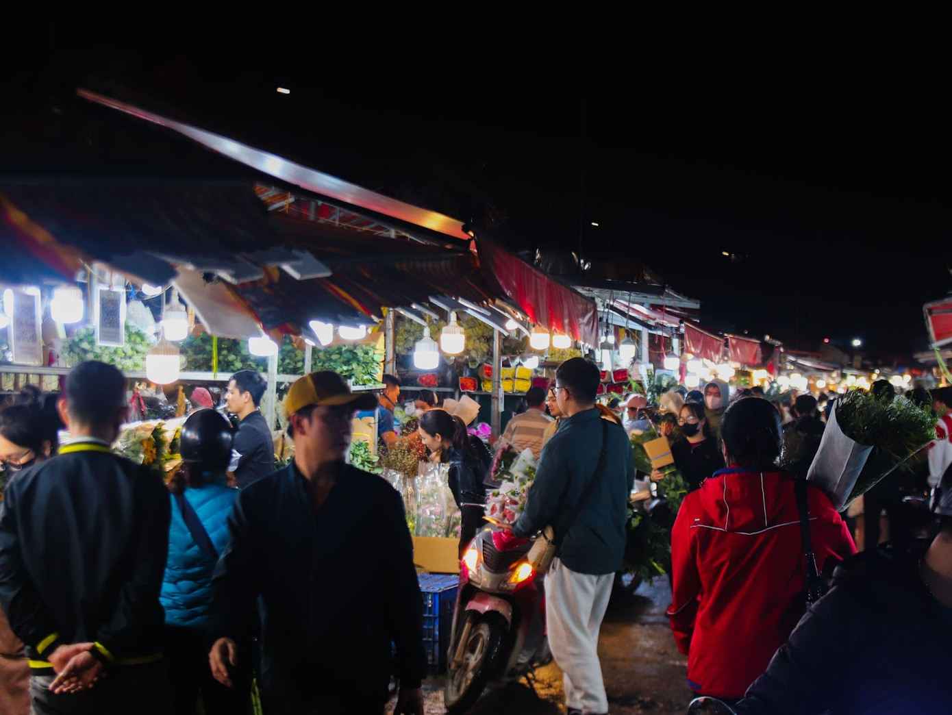 Dù đồng hồ đã điểm 12h đêm, tại chợ hoa Quảng An (quận Tây Hồ, Hà Nội) vẫn rộn ràng tiếng mời chào mua bán của các tiểu thương. Người dân địa phương cho biết, cứ mỗi dịp 8/3 hằng năm, chợ lại trở nên nhộn nhịp hơn bao giờ hết, thu hút đông đảo mọi người đến mua hoa. Trong ảnh là không khí mua bán tấp nập tại chợ hoa Quảng An về đêm. Ảnh: Thu Hà