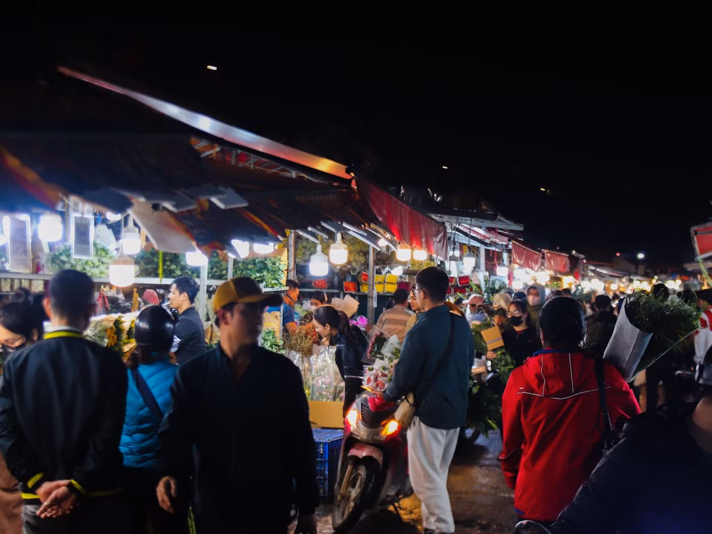 Dù đồng hồ đã điểm 12h đêm, tại chợ hoa Quảng An (quận Tây Hồ, Hà Nội) vẫn rộn ràng tiếng mời chào mua bán của các tiểu thương. Người dân địa phương cho biết, cứ mỗi dịp 8/3 hằng năm, chợ lại trở nên nhộn nhịp hơn bao giờ hết, thu hút đông đảo mọi người đến mua hoa. Trong ảnh là không khí mua bán tấp nập tại chợ hoa Quảng An về đêm. Ảnh: Thu Hà