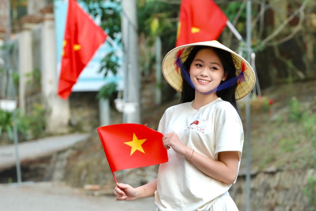Bạn trẻ khoác lên mình chiếc áo với dòng chữ Độc Lập - Tự Do - Hạnh Phúc và đội nón lá truyền thống check-in con đường cờ hoa.