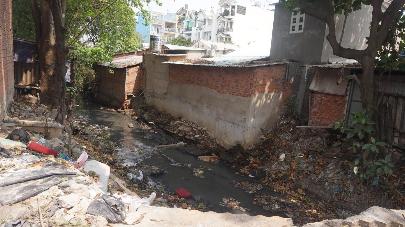 Dòng chảy con kênh bị cản lại bởi rác và những căn nhà xây dựng lấn chiếm.
