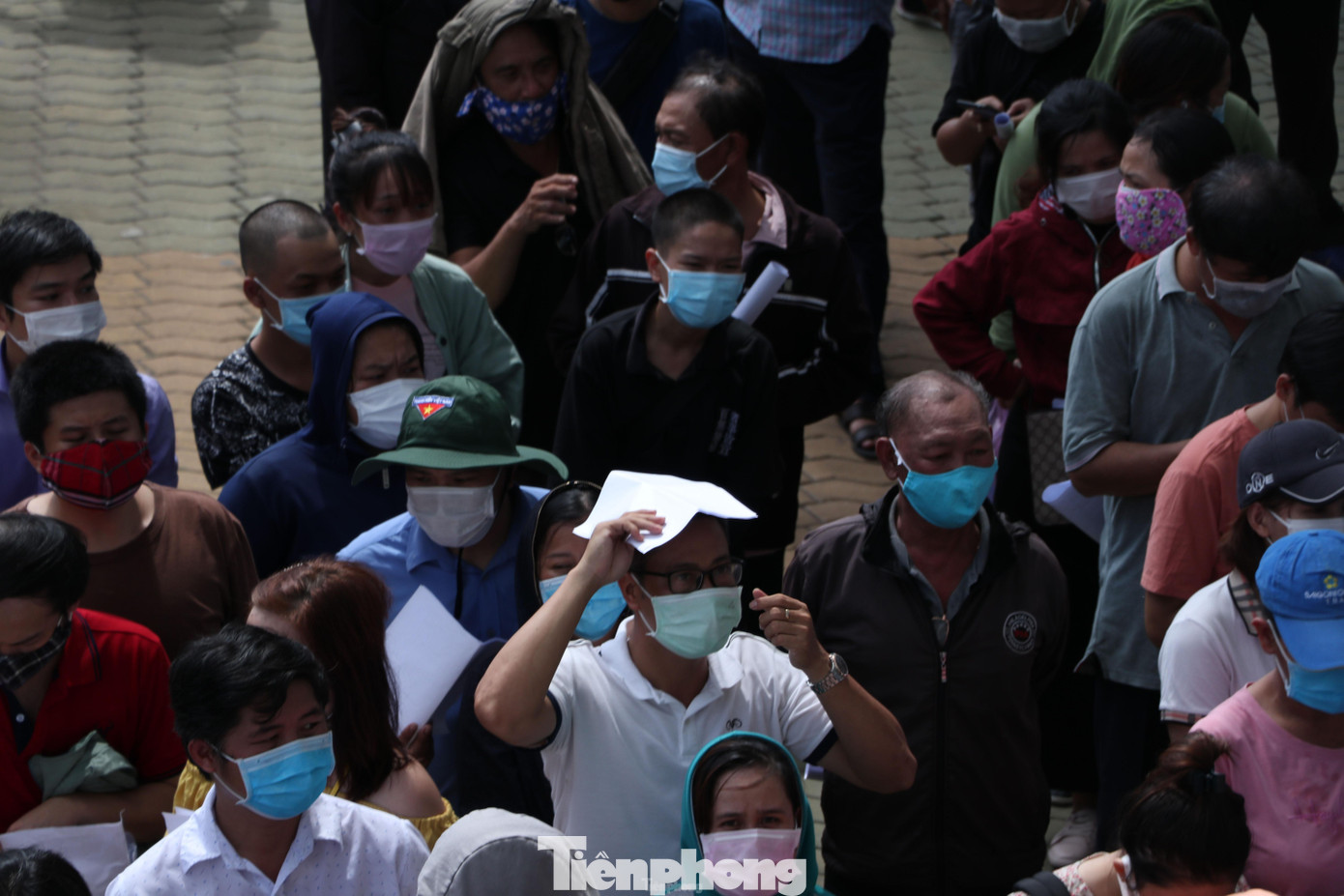 Đứng đợi dưới thời tiết nắng nóng, người dân phải tận dụng giấy đăng ký tiêm để che nắng. Đứng đợi dưới thời tiết nắng nóng, người dân phải tận dụng giấy đăng ký tiêm để che nắng.