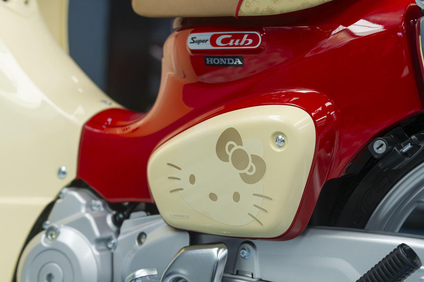 Honda Super Cub Hello Kitty sở hữu phối màu đỏ và be. Logo mèo Hello Kitty xuất hiện trên nhiều vị trí như ốp hông, yếm xe phía trước, bọc yên bằng da, chìa khóa cơ, đồng hồ tốc độ dạng analog kết hợp màn hình kỹ thuật số.