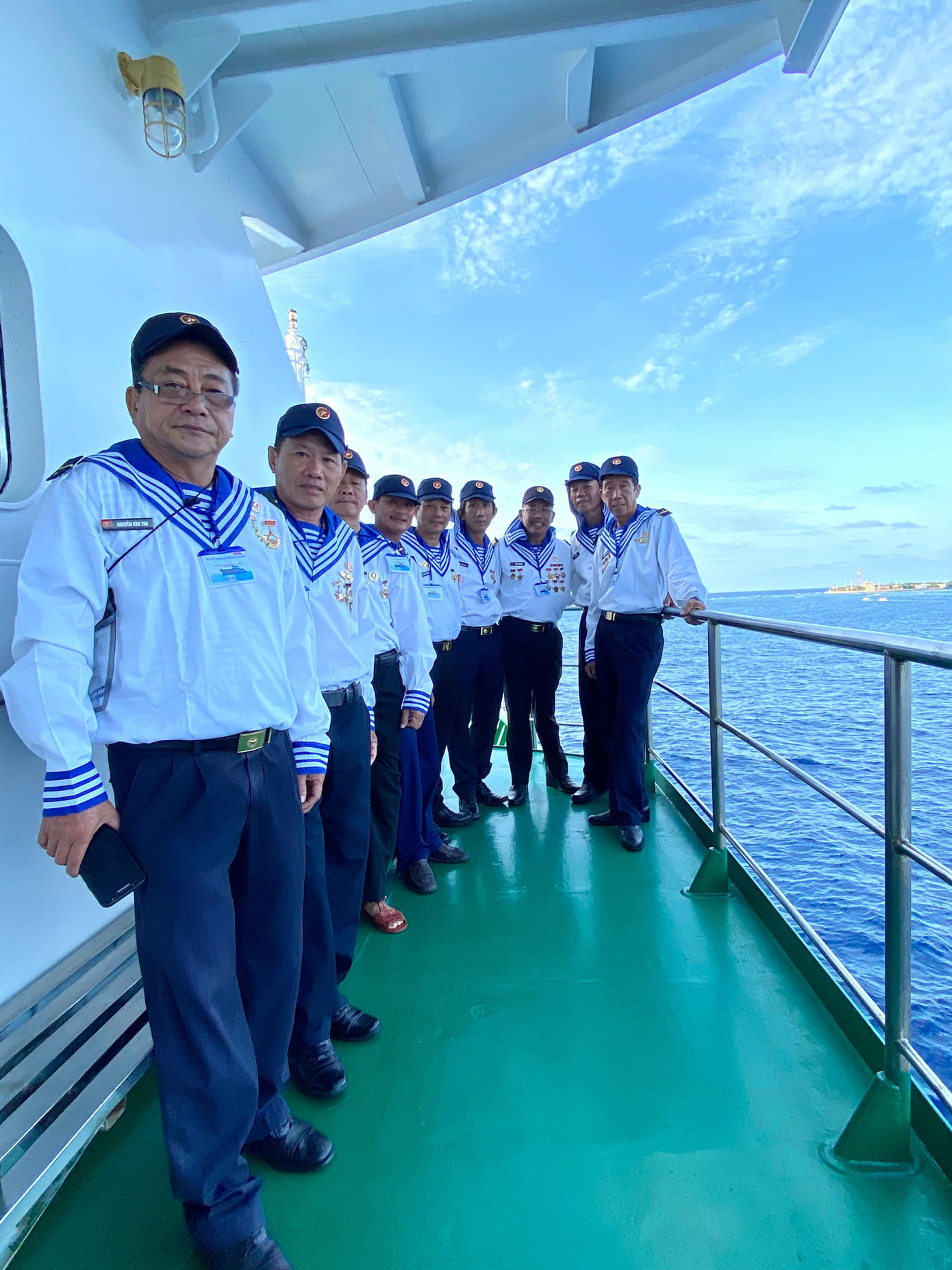 Nhóm cựu chiến binh Trường Sa Đông trên lan can tàu HQ 571 chuẩn bị lên đảo. Phía sau, bên phải họ là đảo Trường Sa Đông