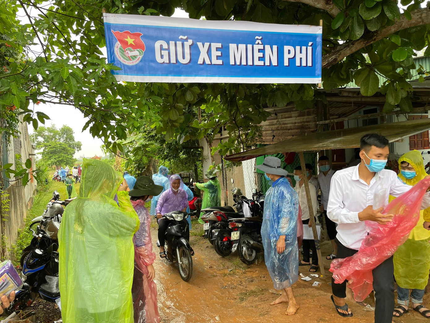 Hình ảnh tình nguyện viên xắn quần, đội mưa để hỗ trợ điểm giữ xe miễn phí cho các thí sinh.