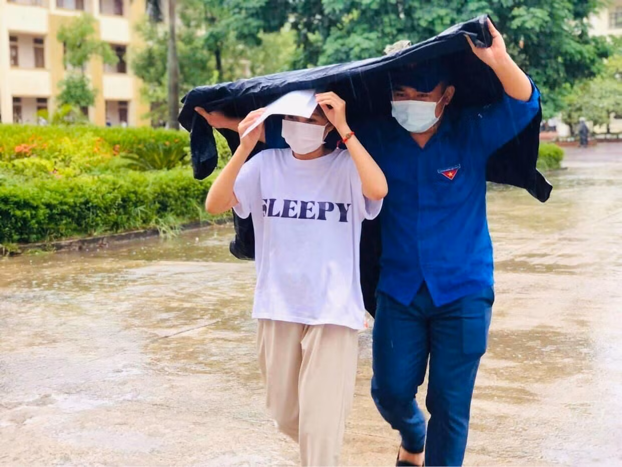 Nam thanh niên lấy áo mưa che cho thí sinh sau giờ thi môn Ngữ Văn để tránh bị ướt.
