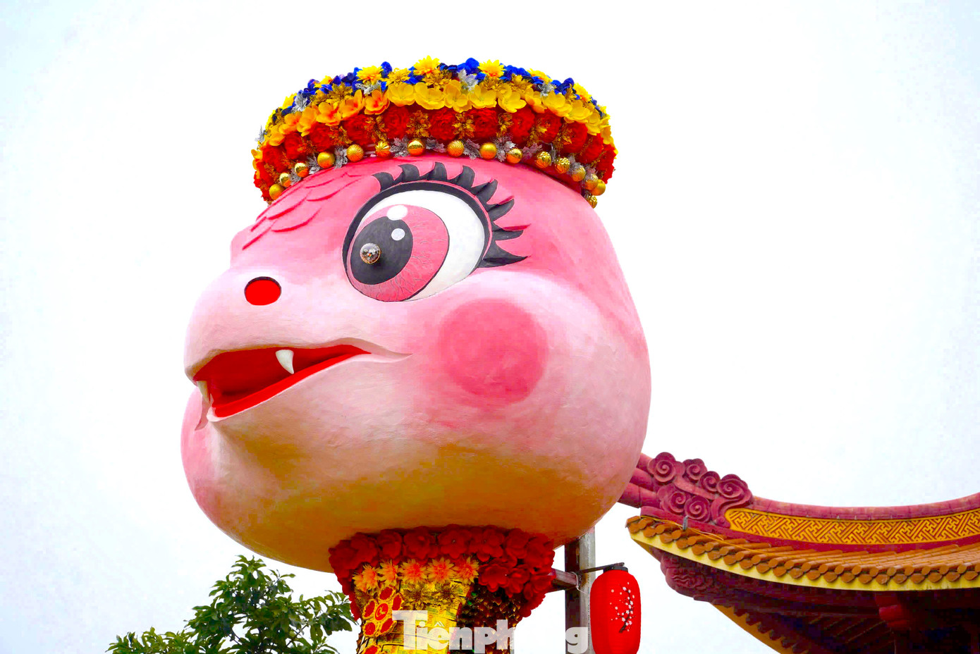 Phần đầu linh vật màu hồng, mắt long lanh, đội vòng hoa.