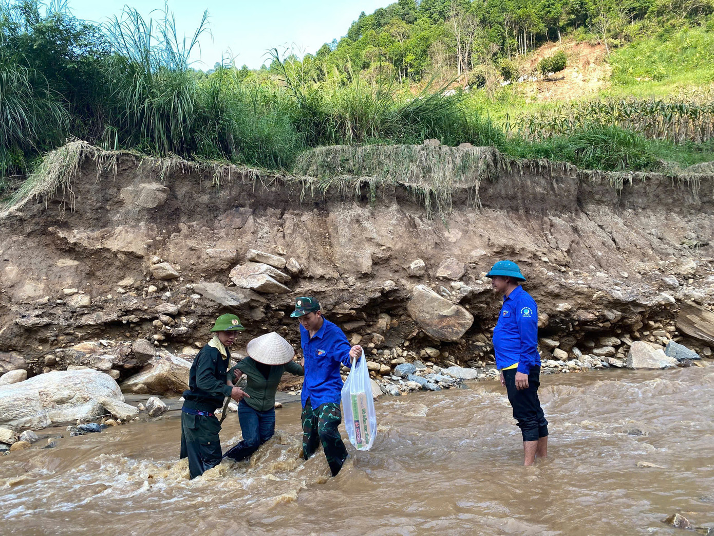 Các thành viên trong đoàn hỗ trợ nhau vượt suối, mang nhu yếu phẩm vào bản Ngải Trồ.