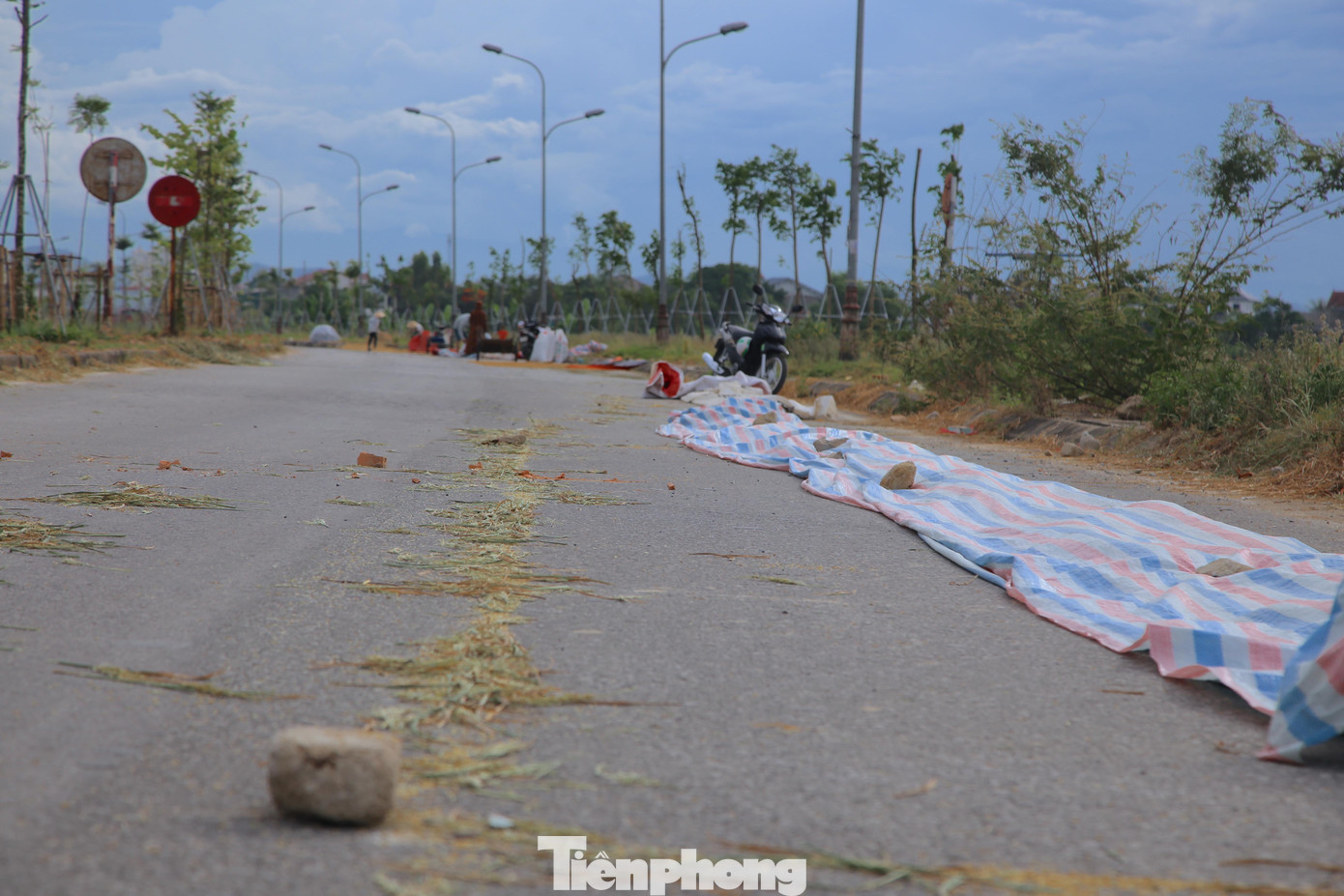 Người dân trải bạt giữa đường để phơi lúa, những phiến đá được đặt tại các góc để tránh bị gió bay. Tuy nhiên việc này gây ảnh hưởng đến giao thông qua lại tại tuyến đường.