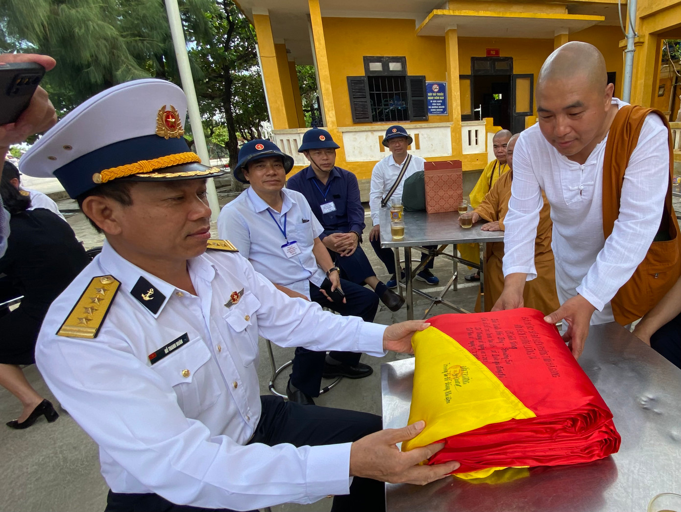 Cư sĩ Vũ Đình Lâm chuyển cho Đại tá Hồ Thanh Hoàn lá cờ Đồn Biên Phòng Lũng Cú gửi tặng Đảo Sinh Tồn Đông. Đảo Sinh Tồn Đông ngày 27/6/2022. Ảnh Lê Xuân Sơn