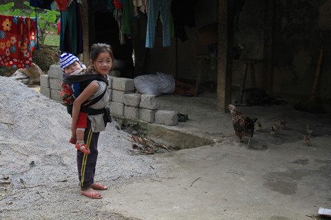 Cô bé ăn mặc phong phanh, địu em giữa trời giá rét. Ảnh: Trường Phong. 