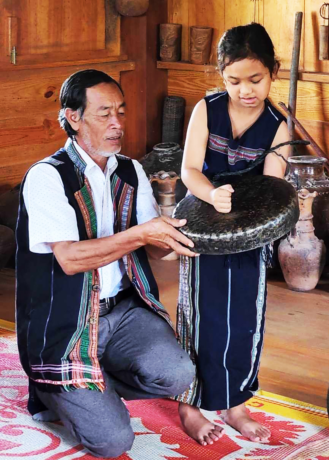 Ông K’Bes dạy bé gái đánh chiêng. Ảnh: Chế Phương Nam