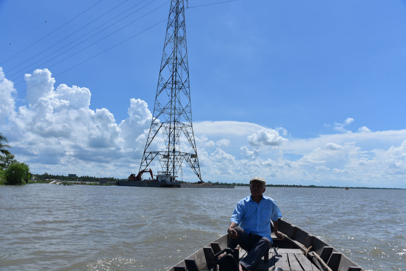 Phía sau ông Hai Nguyên, đất sạt lở, lòi trụ điện 500 kW quốc gia giữa sông Cổ Chiên. Ảnh: Hòa Hội