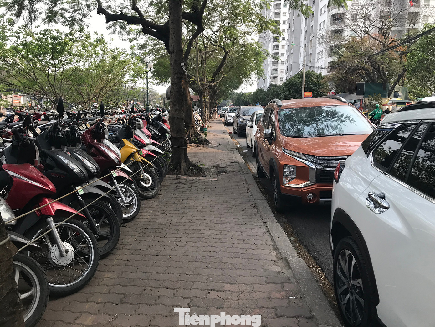 Một đoạn vỉa hè dài hàng trăm mét đầu đường Tam Trinh, giáp bờ sông Kim Ngưu lâu nay bị quây lại để làm bãi trông giữ xe máy. Dưới lòng đường cạnh đó, ô tô dừng đỗ gần như chiếm trọn một phần làn đường. Ảnh: Trường Phong. Một đoạn vỉa hè dài hàng trăm mét đầu đường Tam Trinh, giáp bờ sông Kim Ngưu lâu nay bị quây lại để làm bãi trông giữ xe máy. Dưới lòng đường cạnh đó, ô tô dừng đỗ gần như chiếm trọn một phần làn đường. Ảnh: Trường Phong.