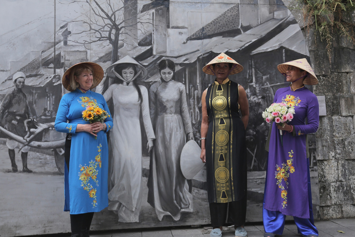 Ba du khách nước ngoài trong trang phục áo dài của Việt Nam chụp ảnh cùng bức bích hoạ trên phố Phùng Hưng. Ảnh: Duy Phạm