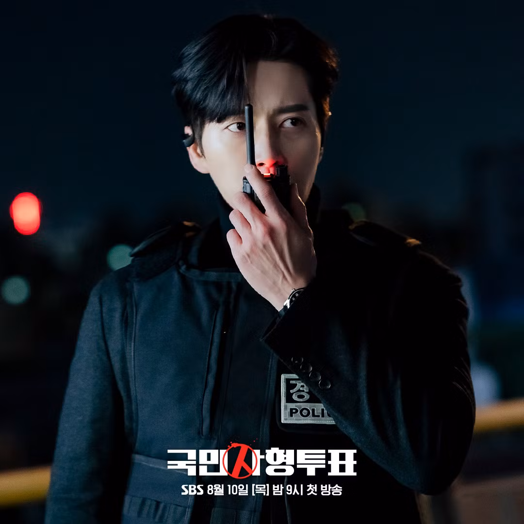 Kim Moo Chan (Park Hae Jin) mặc áo chống đạn đang giao tiếp với ai đó bằng bộ đàm. Đôi mắt sắc bén của anh ấy gợi ý về sự nghiêm trọng tại chỗ.