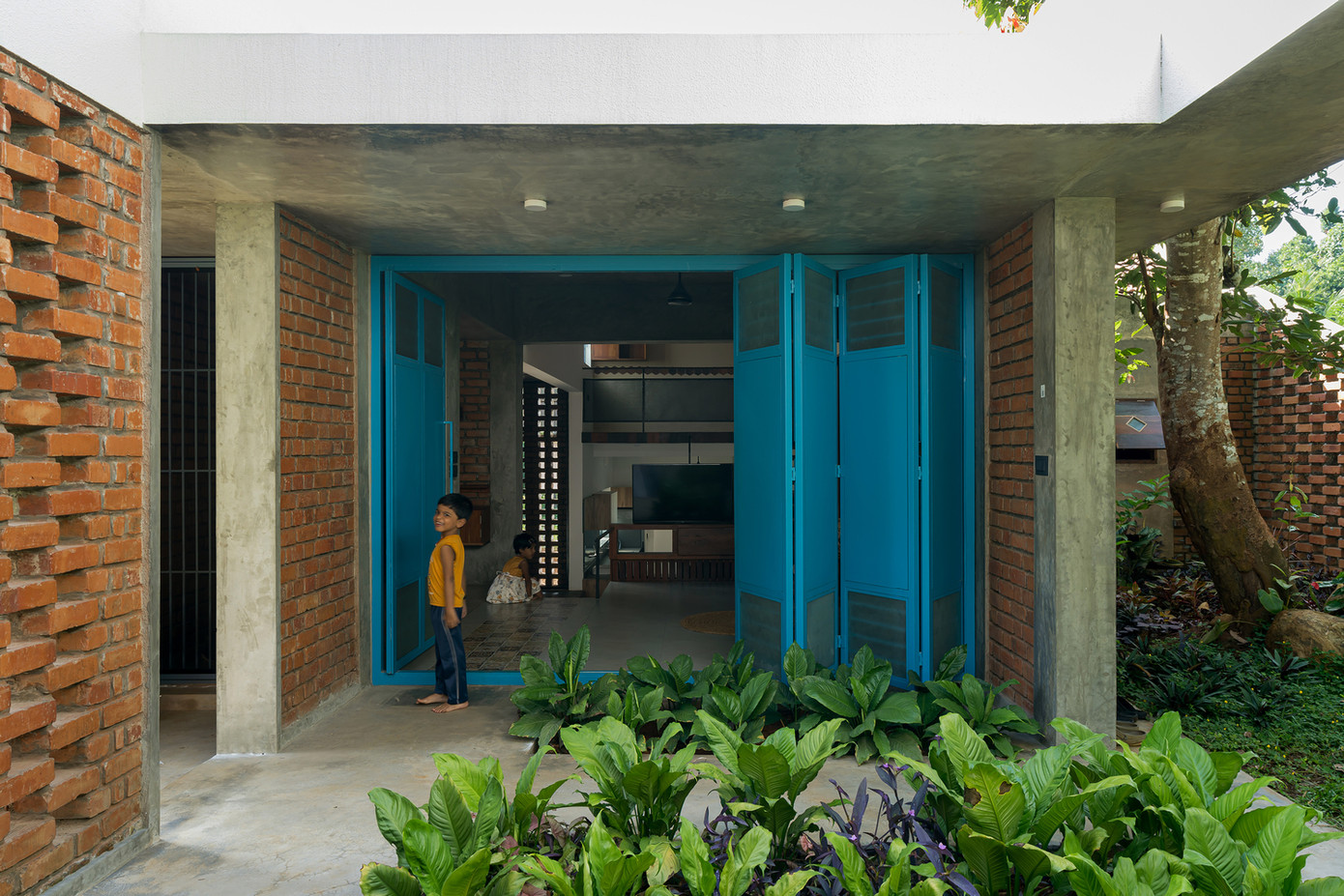 Lối vào nhà luôn thoáng mát và rợp bóng cây nhờ sự kết hợp giữa bức tường gạch xốp màu đỏ với cây cối.