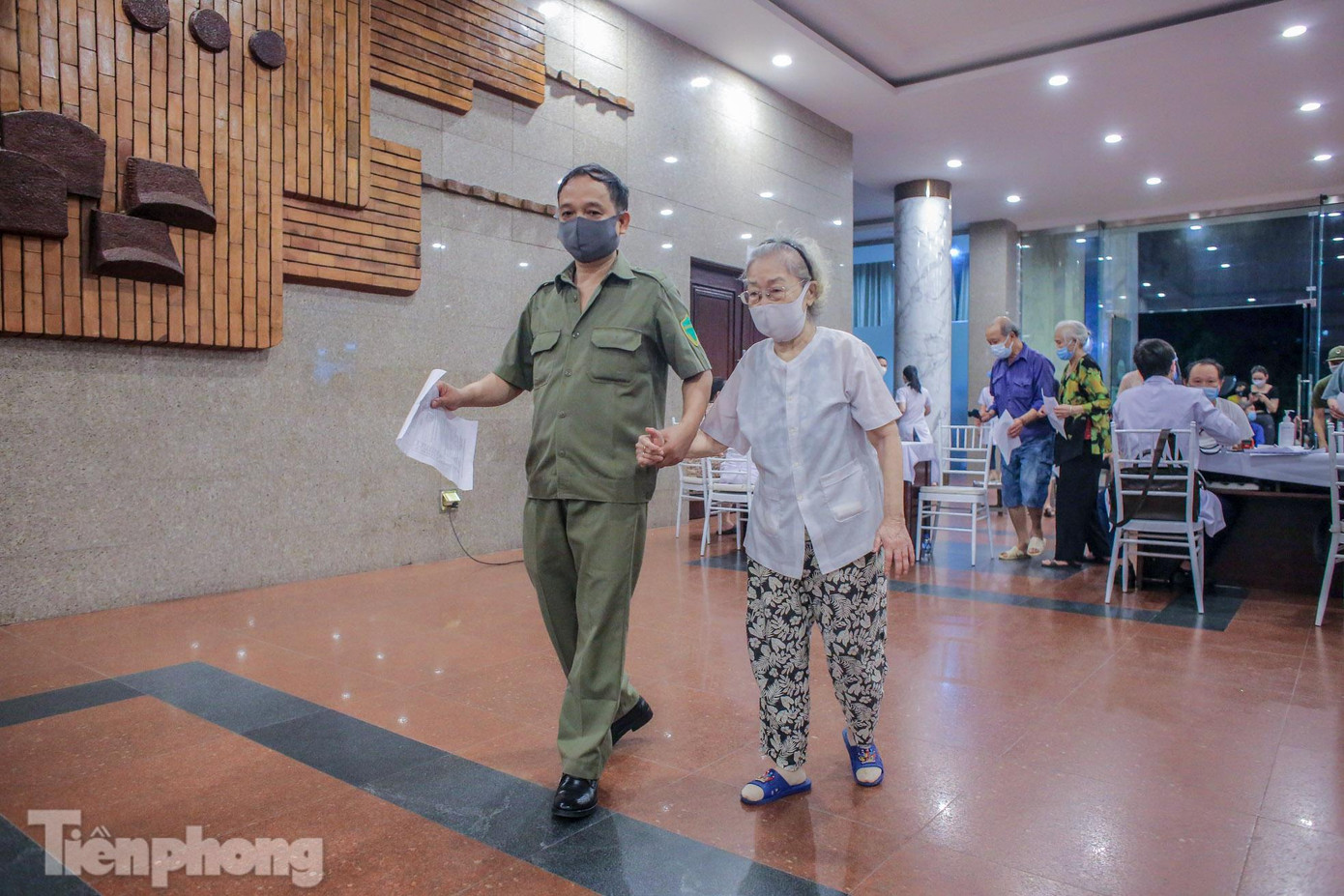 Lực lượng chức năng, bảo vệ tình nguyện viên hướng dẫn, giúp đỡ những người trên 65 tuổi trong quá trình tiêm vắc xin tại đây.
