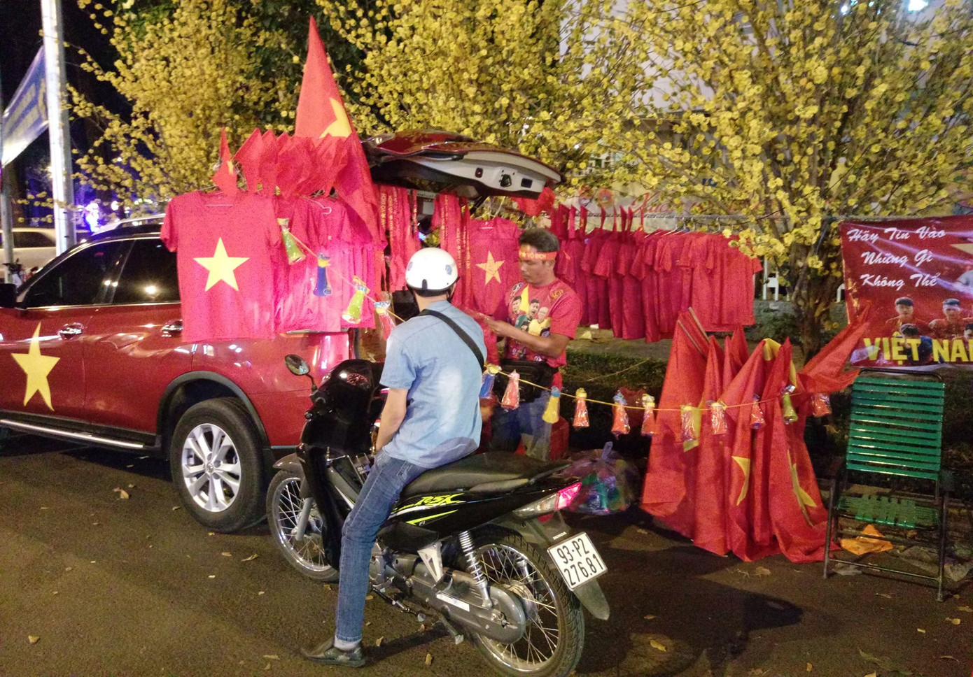 Tận dụng ô tô để bày bán các vật dụng cổ động tại khu vực trước Nhà văn hóa Thanh niên TPHCM. Tại đây, có bố trí màn hình Led cỡ lớn phục vụ người hâm mộ xem trận Việt Nam-Nhật Bản. Ảnh: Nguyễn Tùng