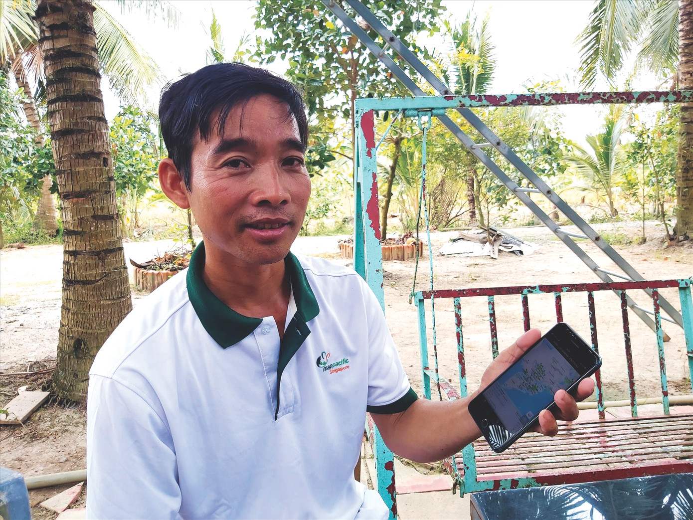 Anh Nguyễn Phước Hưng ngồi nhà cầm trên tay chiếc smartphone theo dõi tình hình sâu bệnh trên lúa của mình. Ảnh: Hòa Hội.