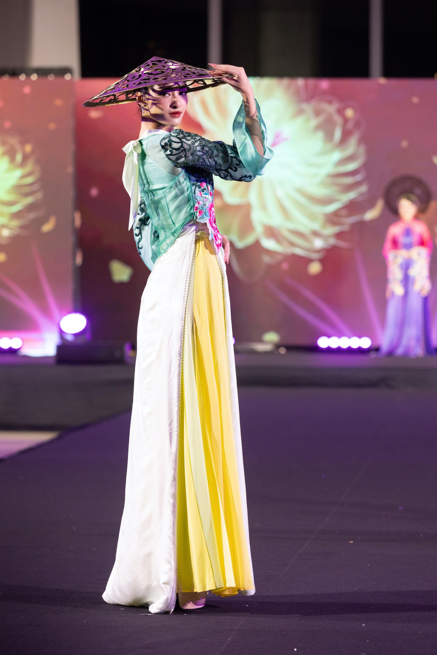 Á hậu Kiều Loan trình diễn thiết kế áo dài nhiều lớp, đính hoa cầu kỳ. Điểm nhấn là chiếc mũ đội đầu có tạo hình giống nón lá.