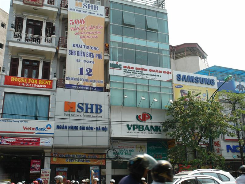 Một dãy cửa hàng, đại lý điện máy, điện tử, chi nhánh các ngân hàng, đại lý điện thoại di động…, vẫn hầu như che kín trên đường Điện Biên Phủ - nơi cấm quảng cáo. Những quảng cáo có chiều cao lớn hơn 2 mét như trong ảnh cũng sẽ vi phạm quy định mới nếu được treo trước các tòa nhà có mặt tiền nhỏ hơn 10m.