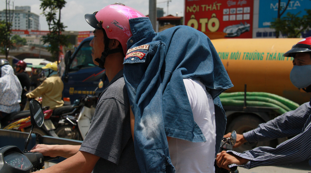 Một phụ nữ lấy áo che đầu trong khi chờ đèn đỏ. Ảnh: Trường Phong