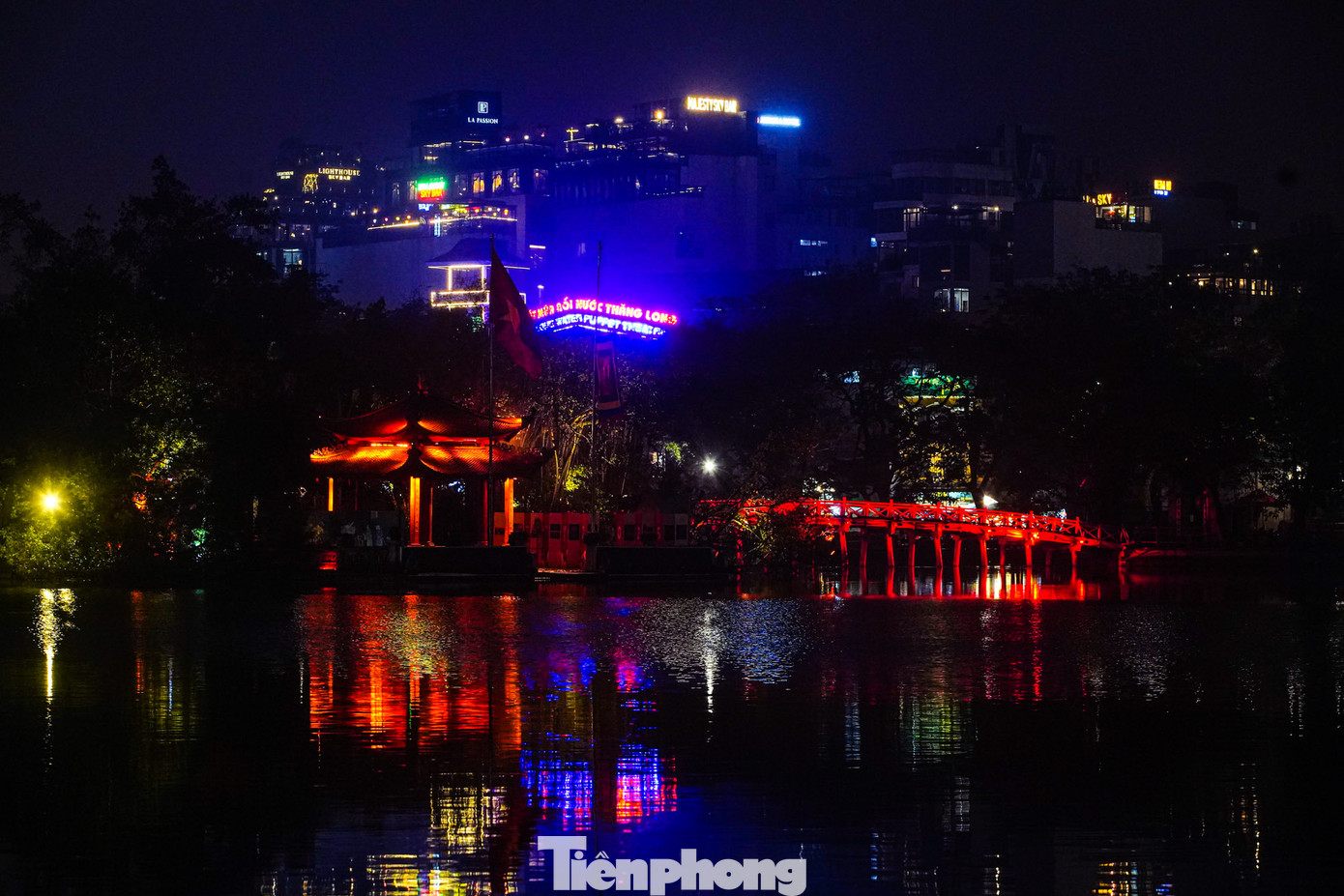 Cầu Thê Húc và đền Ngọc Sơn rực rỡ dưới bóng nước, đằng sau những tòa nhà cao tầng mờ ảo sau lớp sương mù.